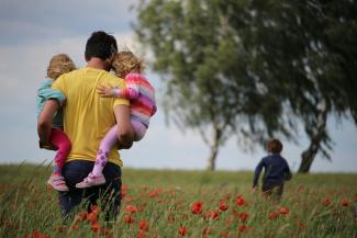 man carrying to girls on field of red petaled flower by Juliane Liebermann courtesy of Unsplash.